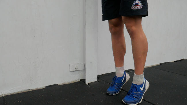 A close-up of a coach demonstrating calf raises from a standing position