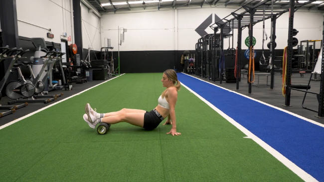A coach demonstrating using a foam roller to release tension on the calves