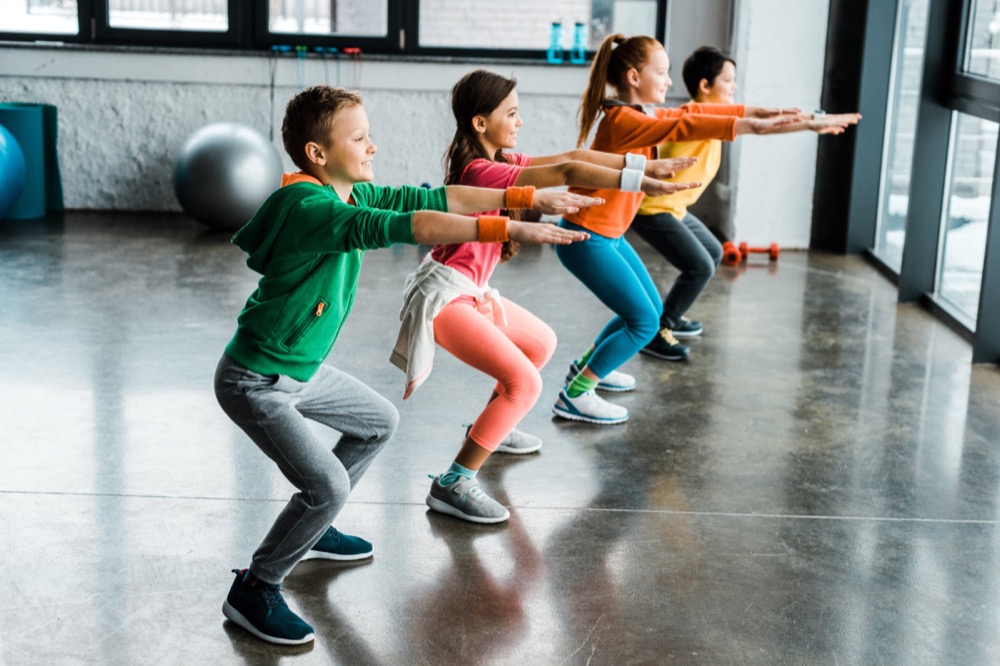 A group of young teenagers practicing bodyweight squat exercises.