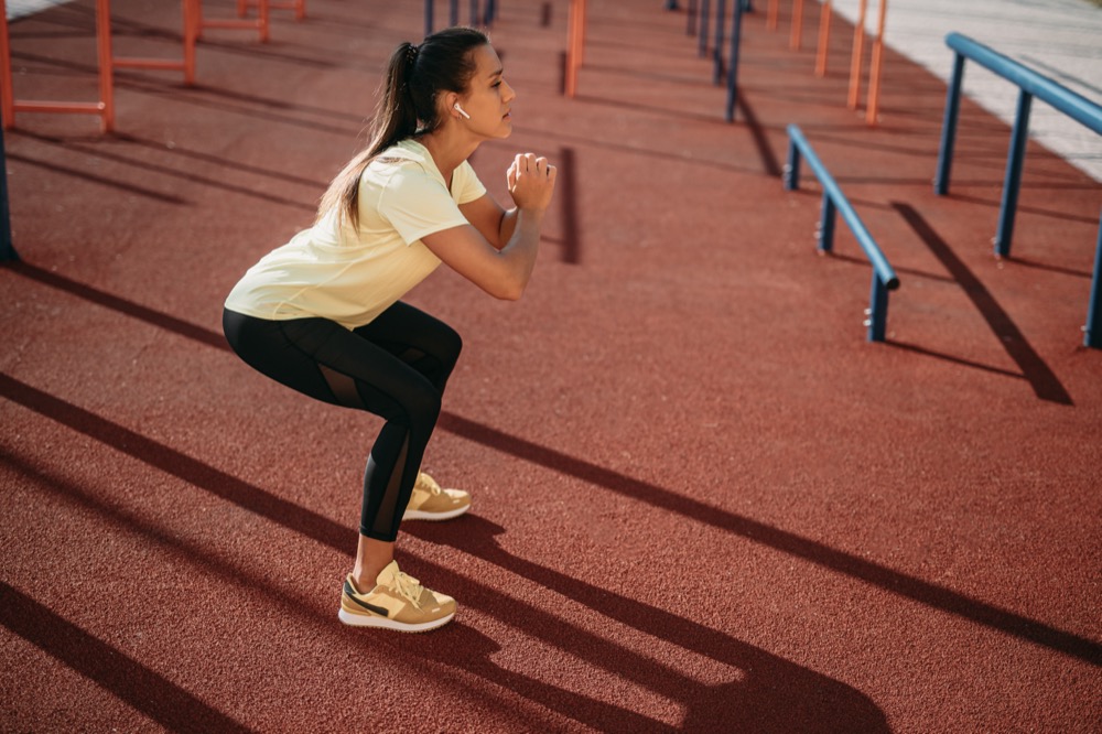A young woman at a sports field doing bodyweight squats.