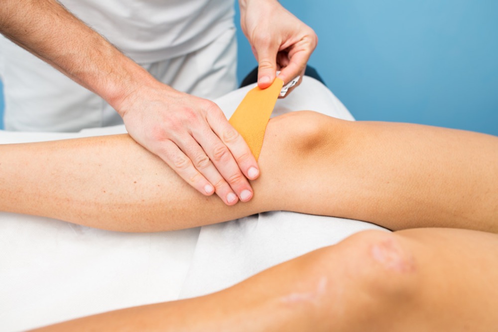 A close up of a therapist apply kinesiology tape to a patients knee