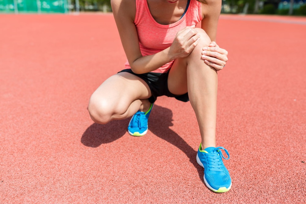 A young athletic woman on a running track clutching her knee