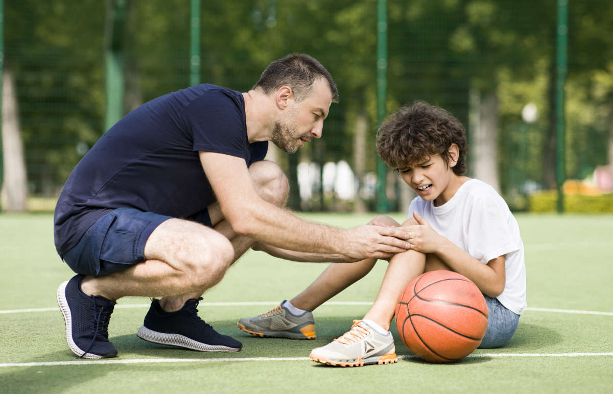 A photograph of a man helping a young teenage boy with a painful knee