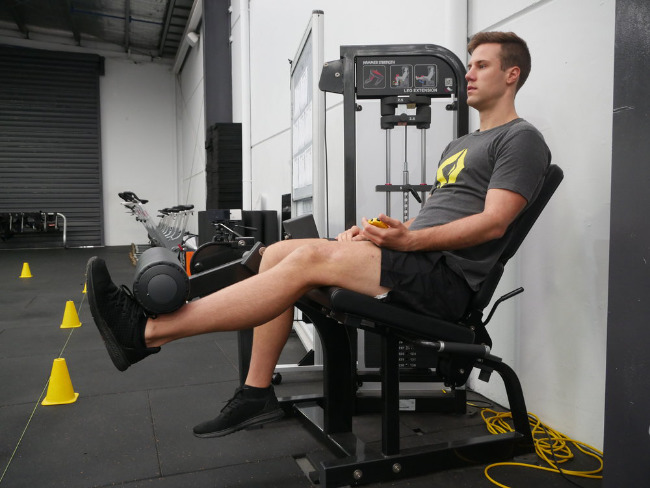 A coach demonstrating a knee isolation hold on a leg extension machine